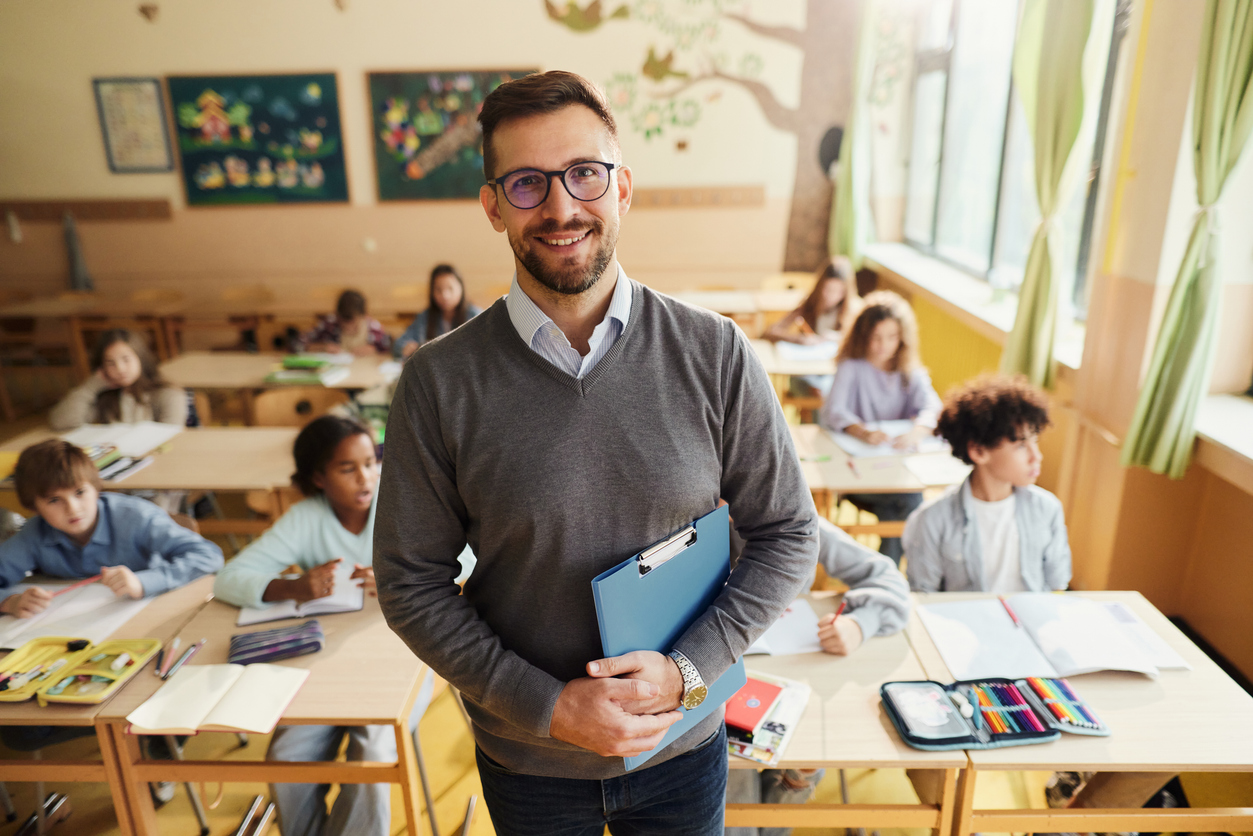 Teacher smiles in his classroom, students in the background